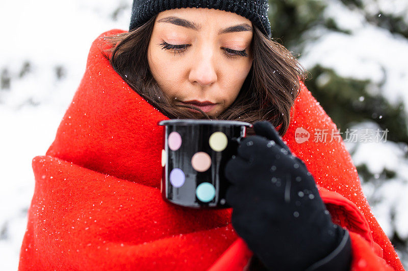 在一个下雪天，一个年轻女子在外喝着一杯茶取暖