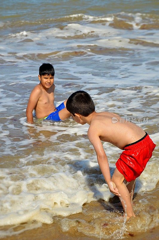 两个男孩在一个夏天的海滩上玩泳裤的海浪垂直图片