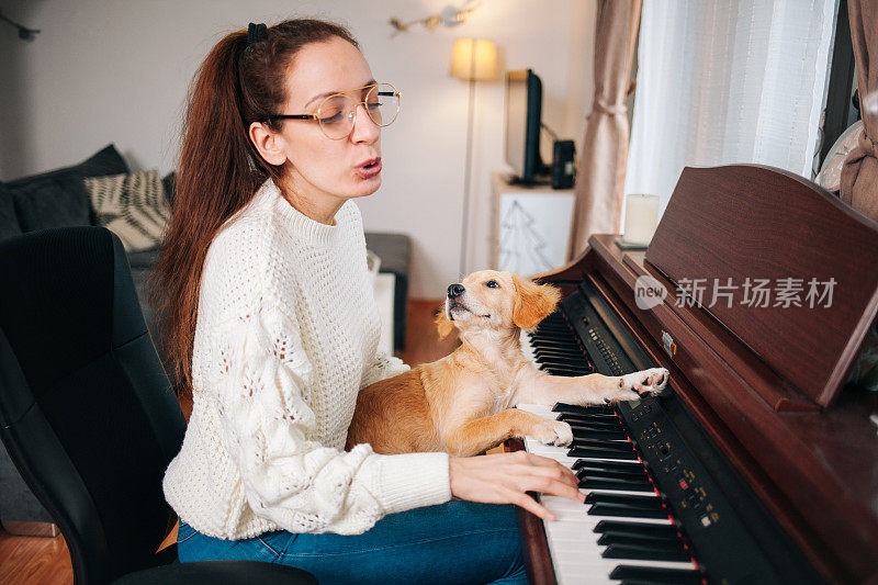 一个女人在练钢琴和唱歌，她的狗躺在她的腿上