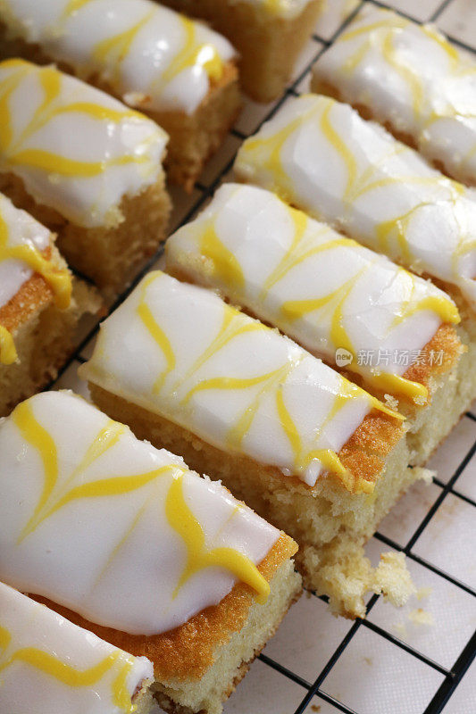 这是自制柠檬蛋糕片的特写图片，上面覆盖着白色的方糖糖霜和羽毛状的黄色柠檬味糖霜，放在金属冷却架上，居高临下的视角