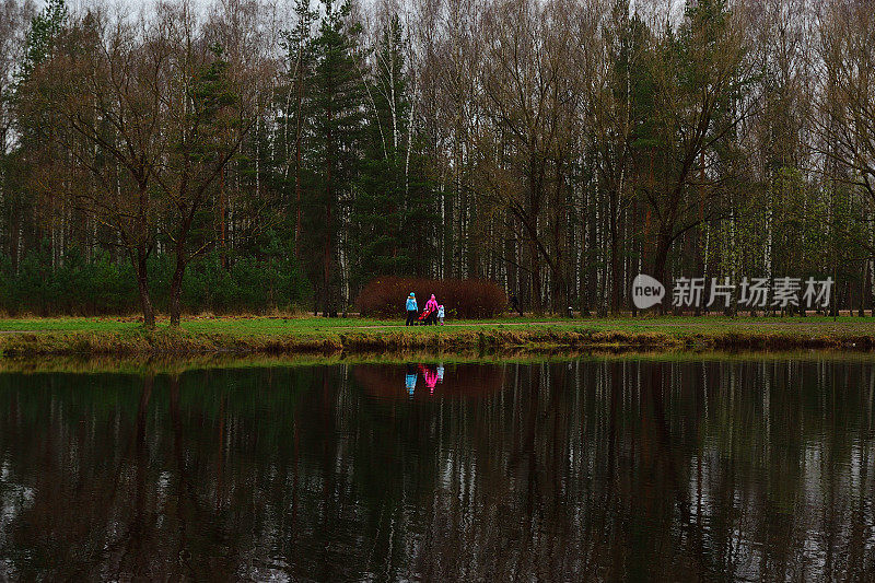 深秋时节，一家人穿着色彩鲜艳的服装沿着池塘边散步。