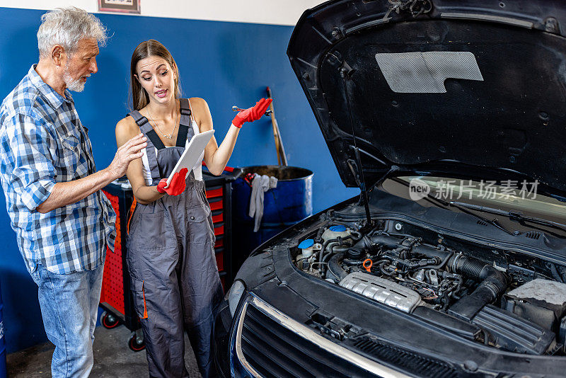 一个资深的汽车维修工和一个年轻的女人在汽车维修厂工作。