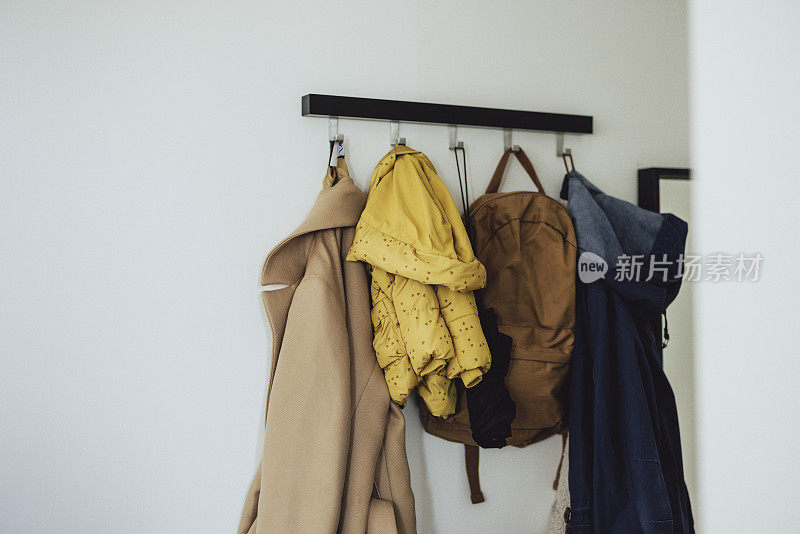 三件夹克和一个背包挂在墙上的架子上