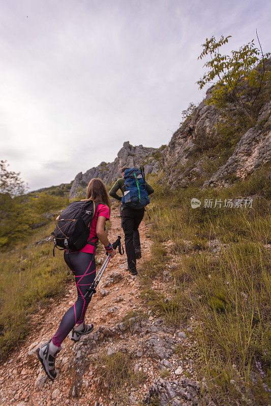 年轻的男女夫妇带着专业的装备和登山杆在美丽的大自然中徒步旅行