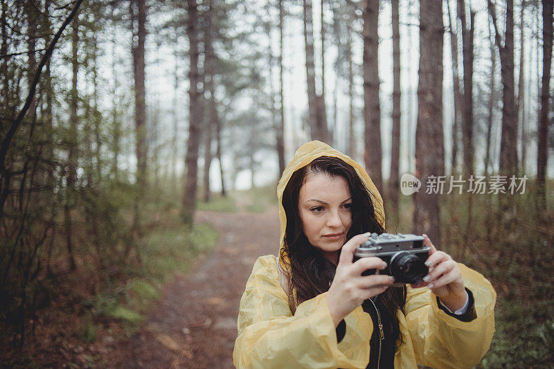 一个快乐的年轻女子在一个下雨天穿着一件黄色雨衣在树林里享受大自然。