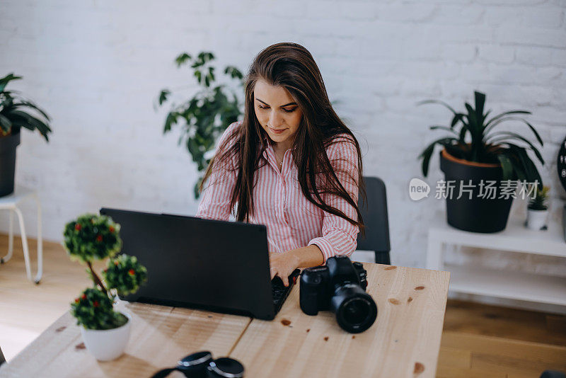 自由摄影师年轻女子在家里用相机在电脑上编辑照片