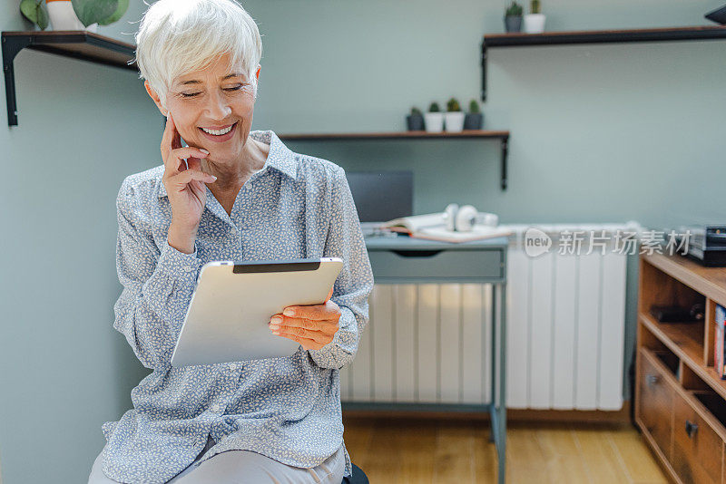 一位高级女性在家中手持数码平板电脑的肖像