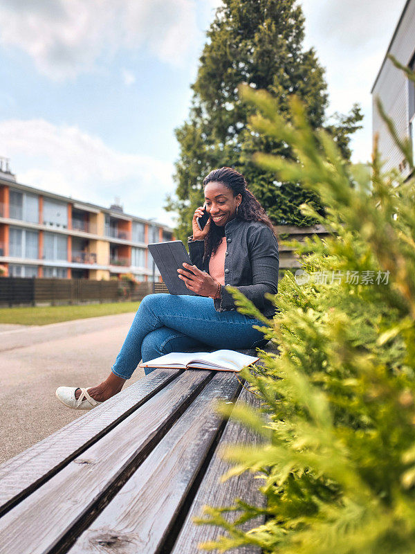 成熟的黑人女性在户外工作，带着数码平板电脑和智能手机