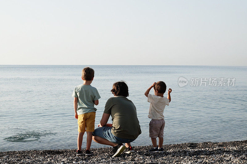 年轻的父亲和他的儿子们在海滩上玩得很开心。父亲节。孩子们拥抱爸爸
