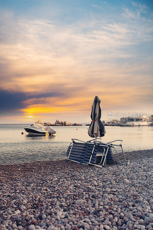 日落时希腊卵石海滩上的封闭式沙滩伞和日光浴床