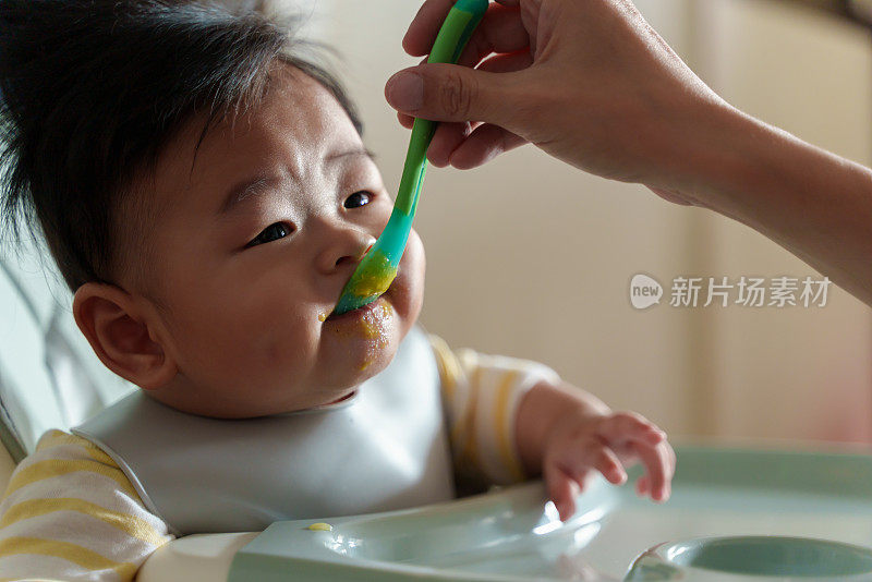坐在高椅子上的亚洲小男孩正在被妈妈喂食。