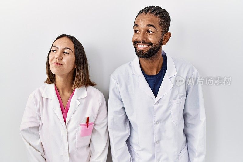 年轻的西班牙裔医生站在白人背景微笑着看向一边，盯着别处思考。
