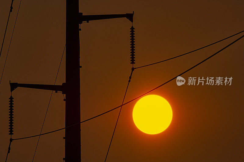 一个炎热的夏天，太阳在高压输电杆后面的特写