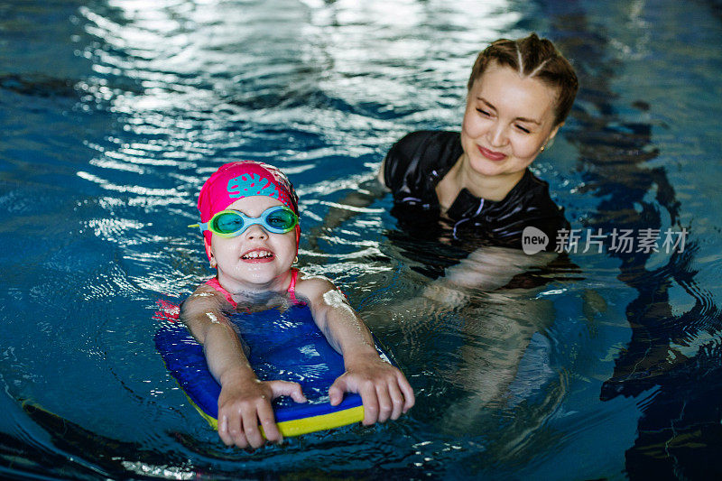 小孩在游泳池里学游泳。游泳教练教学龄前儿童在游泳池游泳