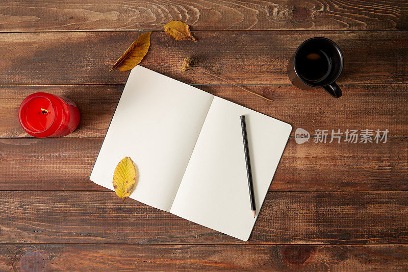 铅笔和笔记本的木制背景与一杯咖啡，蜡烛和秋叶。