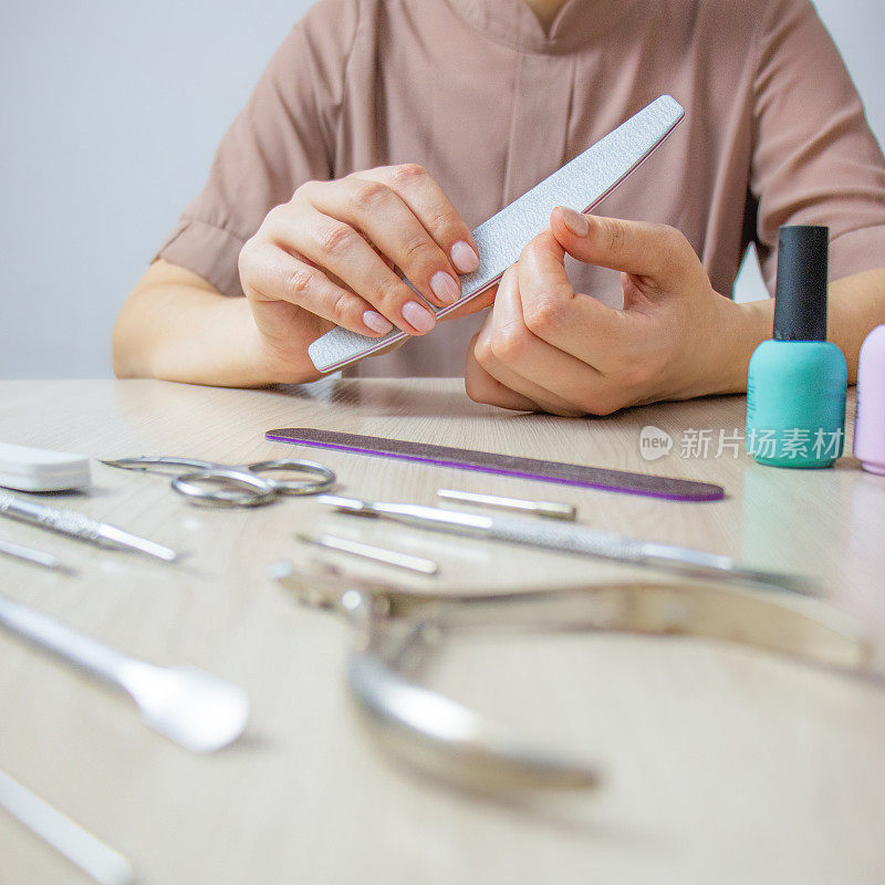 回家修指甲，女人用指甲锉锯指甲，桌上放着修指甲的工具和指甲油