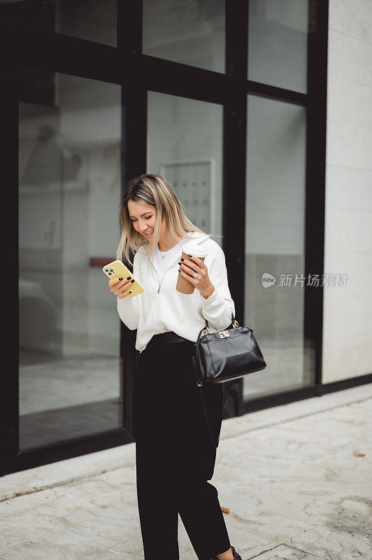 年轻的女博主在户外散步时用手机带走一杯热饮。