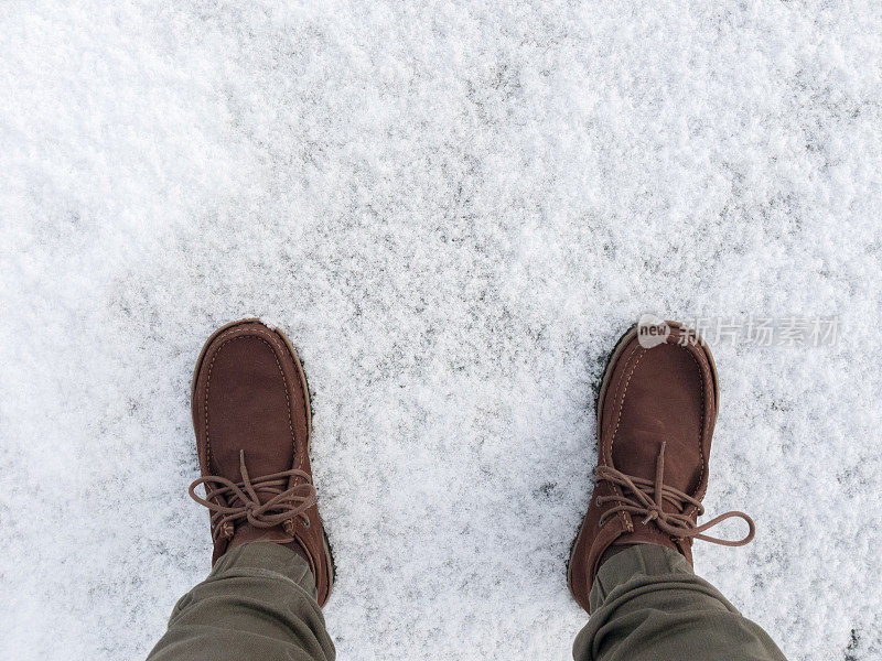 脚穿着靴子走在铺着雪的柏油路上。