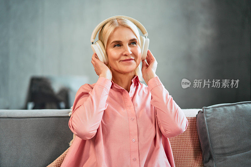 一个穿着粉色衬衫的美丽老妇人的肖像，拿着耳机，微笑着看向别处。