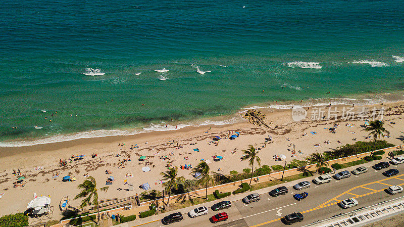 2023年春假期间，佛罗里达州棕榈滩沙滩海岸线上充满蓝色海浪、岩石、海藻、沙滩伞、冲浪板和人们的充满活力的海滩上的空中无人机视图