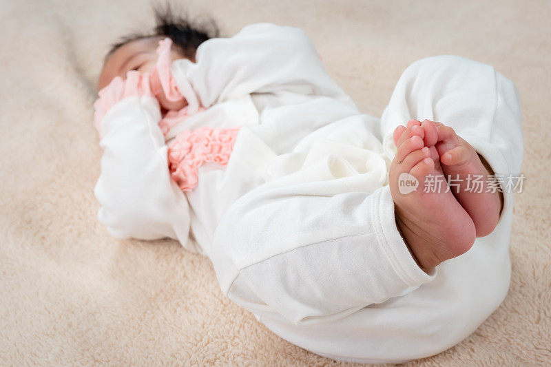 一个3个月大的亚洲婴儿躺在床上，双手舒服地放在嘴边。她从床上醒来，等着妈妈来，脸上挂着幸福的微笑。