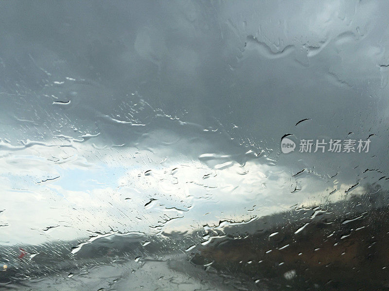 下雨天开车。雨点落在汽车挡风玻璃上，多云的天空和空旷的道路背景