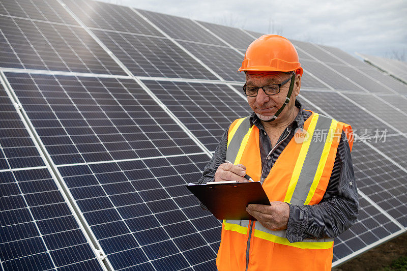在太阳能农场工作的维护工程师，手里拿着一个剪贴板。