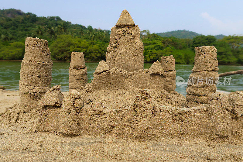 在印度果阿的海滩上建造的复杂沙堡堡垒的图像，用桶和铲子制成，并修改为围绕外部的墙，背景是大海，正面视图