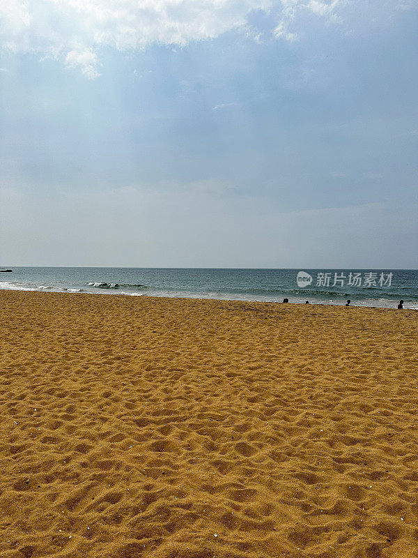 海浪在沙滩上破碎的图像，潮汐和海洋运动，阳光冲破云层，水边偶然的人，壁纸背景，重点在前景，复制空间