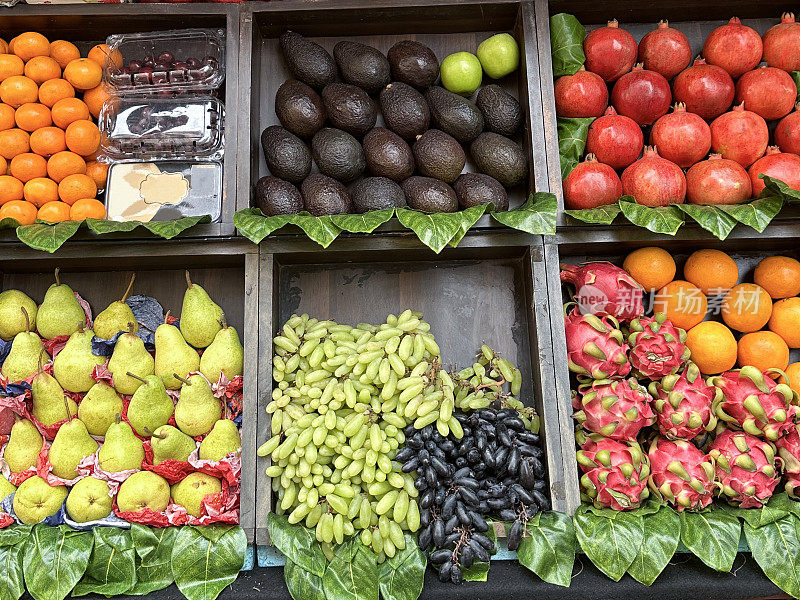新鲜农产品超市木制抽屉的全画幅图像，里面有梨、红葡萄和白葡萄、火龙果、橙子、石榴、苹果、鳄梨、蜜橘和塑料篮樱桃，高架视图