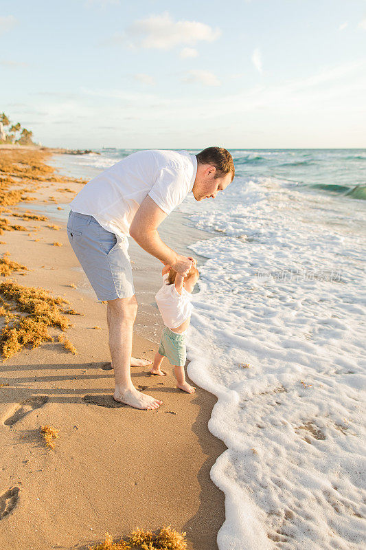 2023年春天，佛罗里达州棕榈滩，一位31岁的美国父亲和他1岁的儿子在沙滩上玩耍，一起享受金色日出的时光