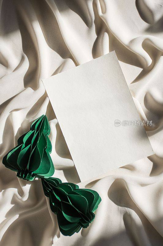 把一张纸折叠起来，放在一张白色的纸上，旁边放着绿色的花