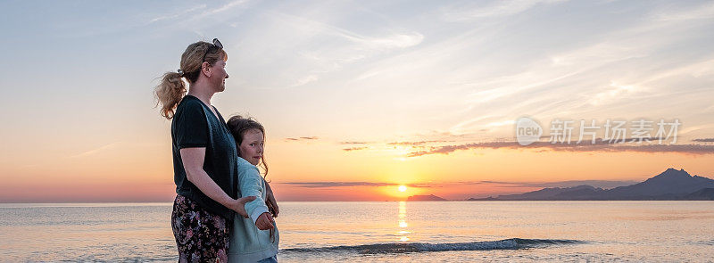 一个白人家庭的肖像，一个8岁的女孩和一个年轻的女人在海上遇见日出。