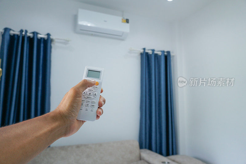 亚洲男人用遥控器关掉客厅的空调。简单的能量在家里。