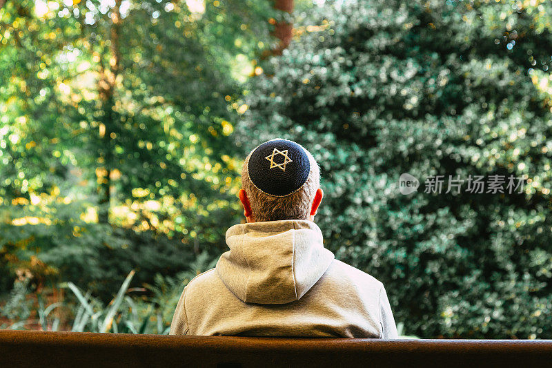 一名犹太男子戴着圆顶小帽坐在公园的长椅上