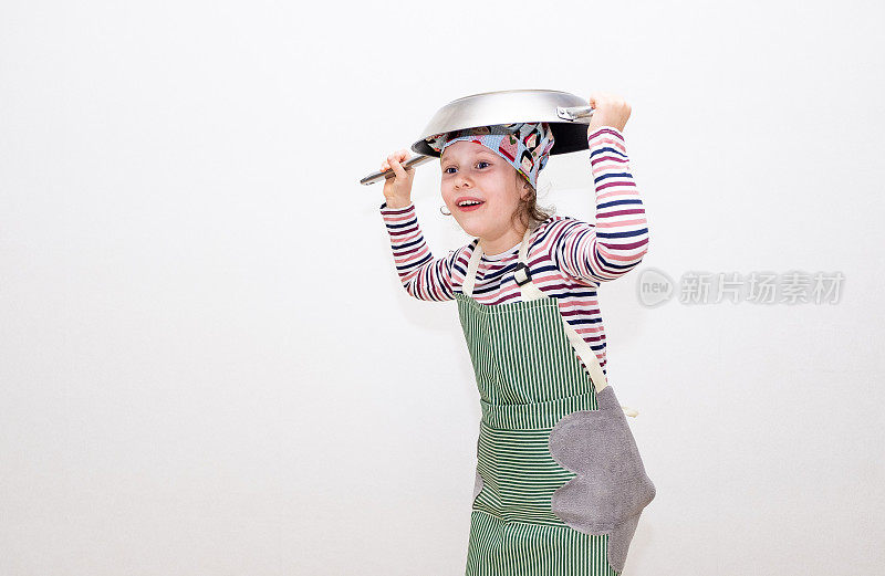 一个8岁的白人女孩打扮成厨师，双手拿着一只大煎锅举过头顶，很开心。