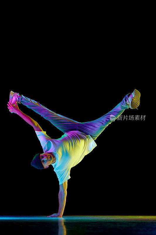 手站。刷卡。年轻灵活的运动员在霓虹灯的黑色背景下，穿着运动服跳霹雳舞。