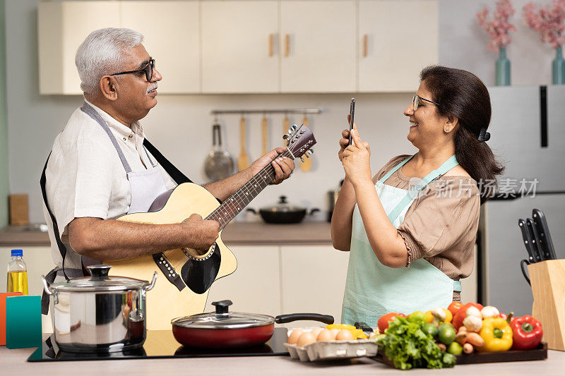 幸福的老年夫妇弹吉他，在家里一起做饭，股票照片
