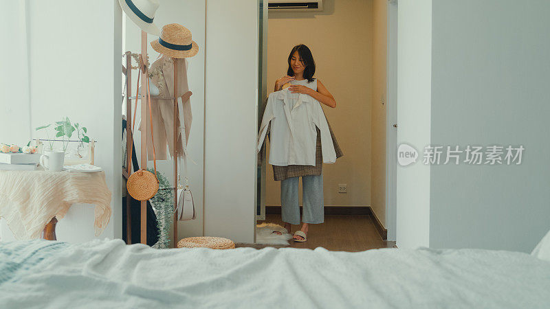 上午晚些时候，年轻的亚洲女子在家里卧室的大衣柜里挑选衣服。日常的生活方式。