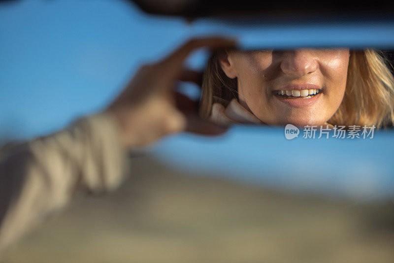 汽车后视镜上一个微笑的女人的倒影