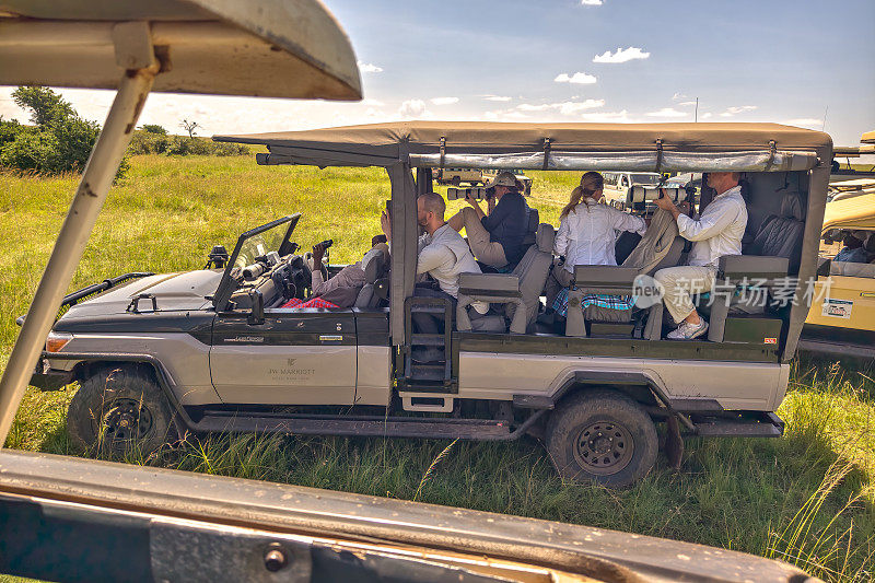 一名游客在肯尼亚的游猎旅行中拍摄野生动物。一名男子在一辆敞篷游猎车上带着相机在非洲旅行。马赛马拉国家公园，肯尼亚。