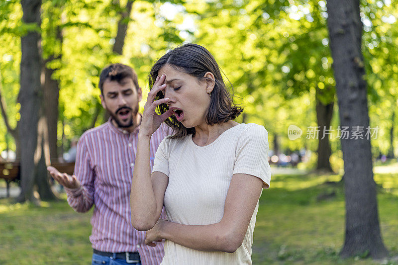 一对年轻夫妇在公园里吵架。年轻夫妇有一个夏天的一天争吵。站在公园外面，困惑的年轻女子打着手势，看着她的男朋友