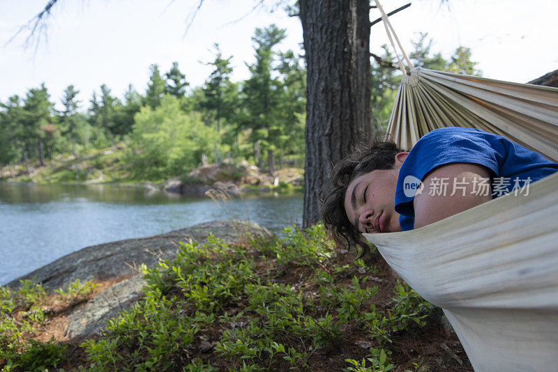 一个十几岁的男孩夏天睡在湖边的吊床上。