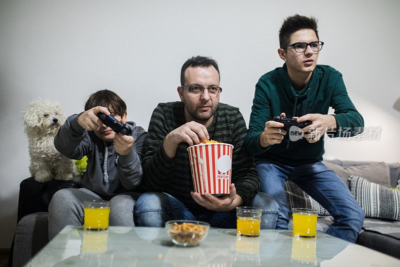 叔叔和他的两个侄子一起玩电子游戏。也可能是父子关系。