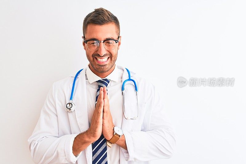 年轻英俊的医生男子戴听诊器在孤立的背景祈祷与手一起请求原谅自信微笑。