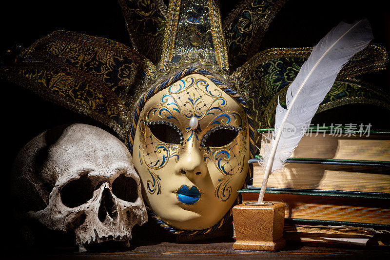 戏剧、文学和戏剧概念。威尼斯面具，旧墨水瓶，羽毛，羽毛笔，书和头骨放在木桌上。古董静物。