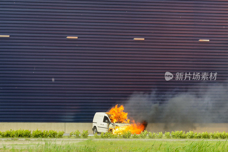 在工业区的一堵工厂墙前燃烧的汽车