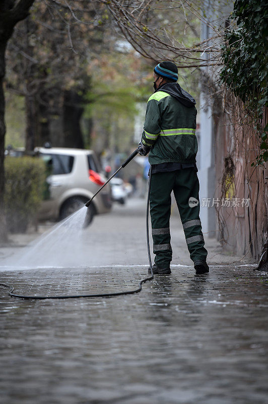 在罗马尼亚首都布加勒斯特，一名公共清洁工在冠状病毒大流行期间用高压消毒剂深度清洁人行道