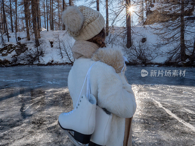 一个年轻女子肩上扛着冰鞋走在结冰的湖面上