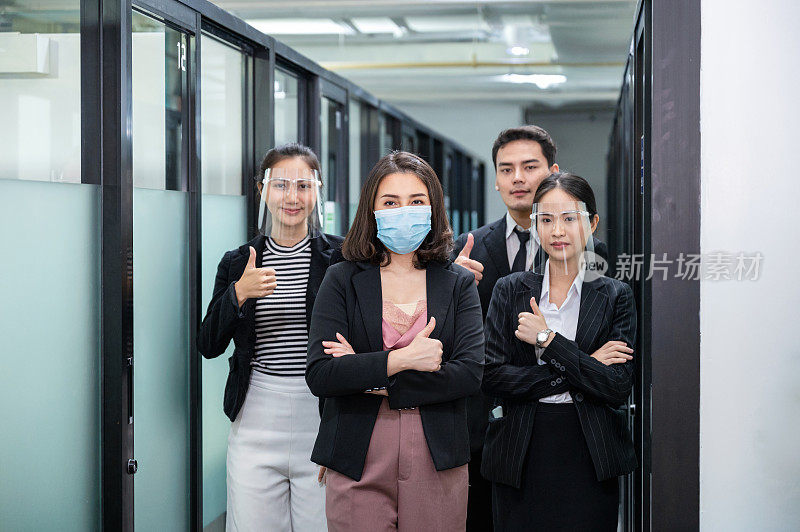 亚洲商务人士戴着面罩，面罩上竖起大拇指在重开办公室